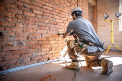 A builder works with a drill at a construction site.